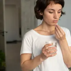 Mujer toma pastilla con agua, pensando en cuando tomar probióticos con antibióticos para cuidar su salud intestinal.