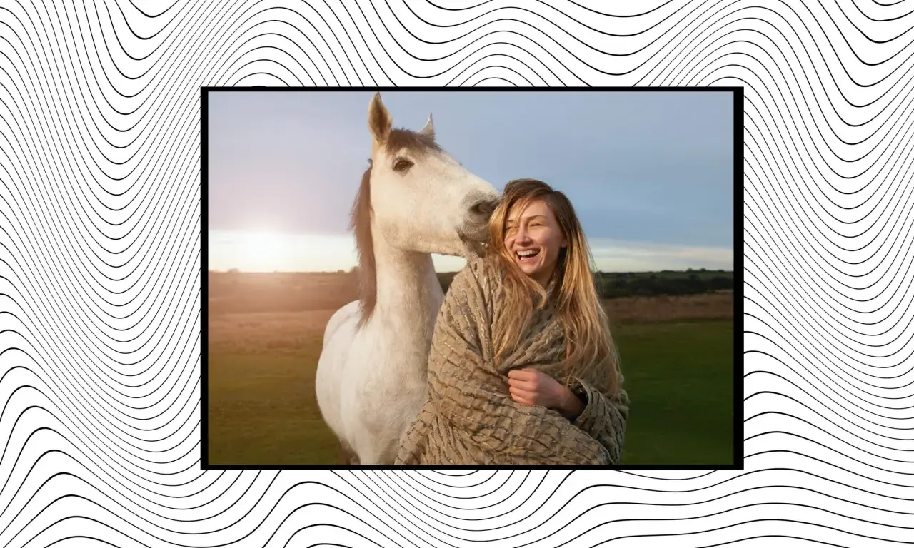 Una mujer ríe mientras un caballo blanco le da un suave mordisco. Es como soñar con un caballo blanco en un campo al atardecer.