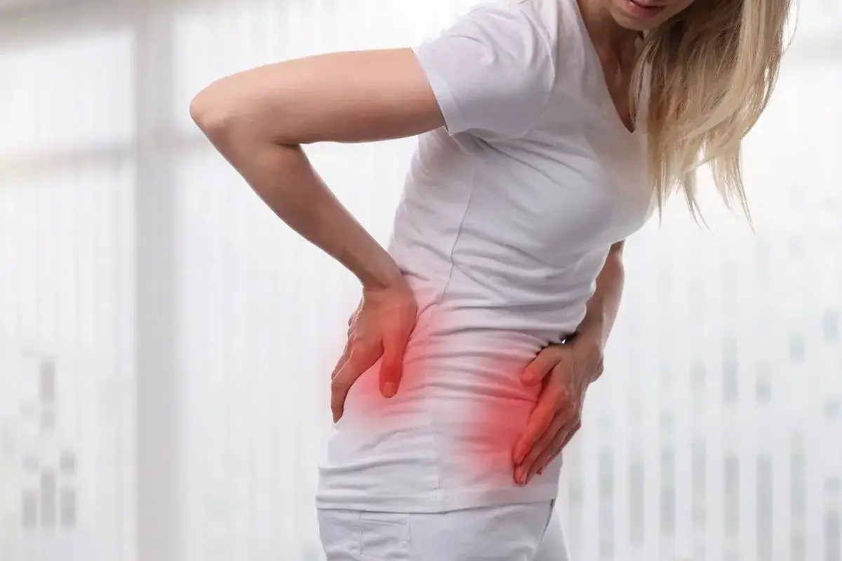 Mujer con dolor de riñones, con las manos en la zona lumbar. Podría ser dolor de riñones regla.